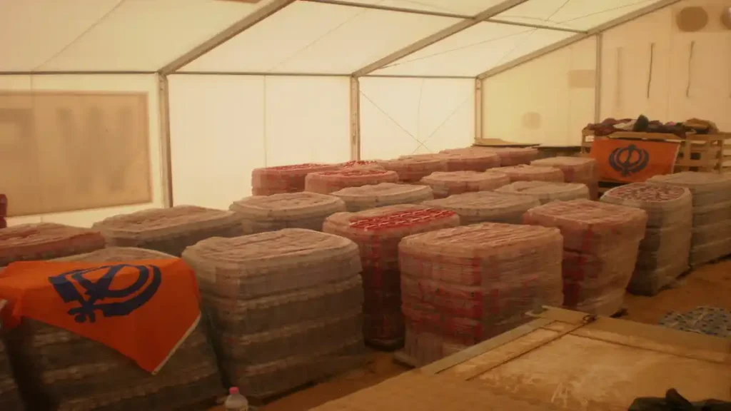 Khalsa Aid relief supplies stored in a large tent with Sikh Nishan Sahib flags