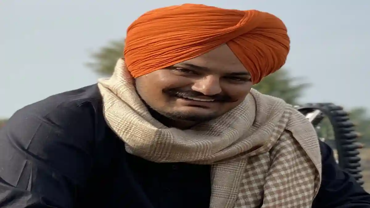 Sidhu Moose Wala smiling and sitting in a field.